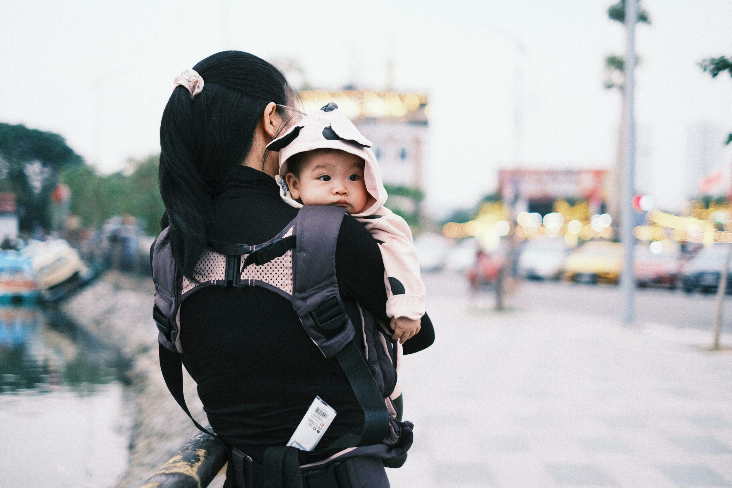 Eine Mutter trägt ihr Baby in einer Trage auf einer Stadtstraße.